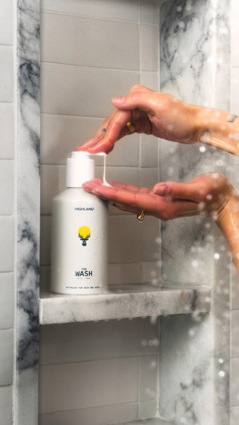 Hands pumping Highland The Wash shampoo into palm on a marble shelf in a tiled shower