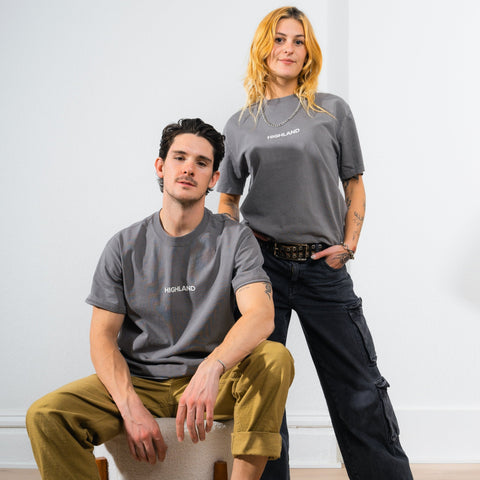 Two models wearing gray Highland Essential tees — one seated, one standing against a plain white background.