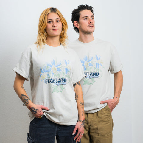 Two models wearing light-gray tees with blue aquilegia floral print and 'HIGHLAND' logo on the chest