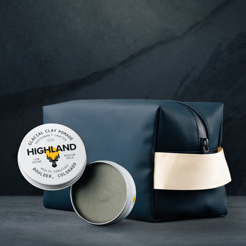 Navy dopp kit beside open tin of glacial clay pomade labeled HIGHLAND