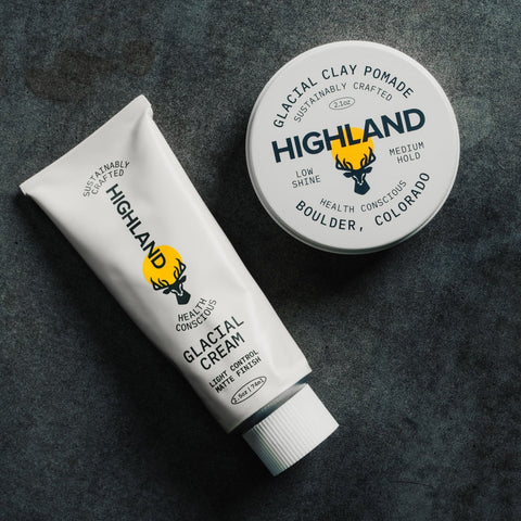 Top-down of Glacial Cream tube and Glacial Clay Pomade tin showing product labels and Highland logo on dark textured surface