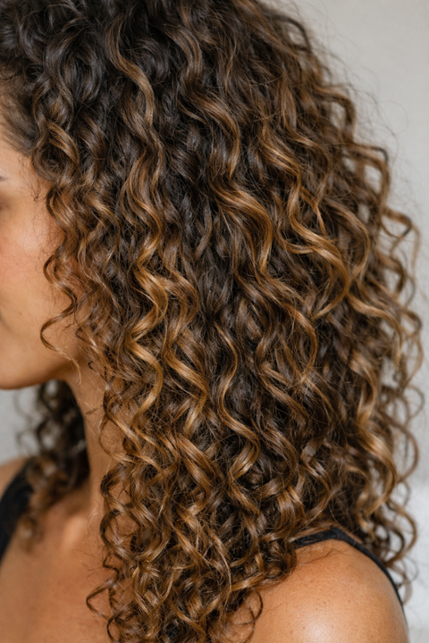 Side profile of a woman with shoulder-length defined brown curly hair against a neutral background