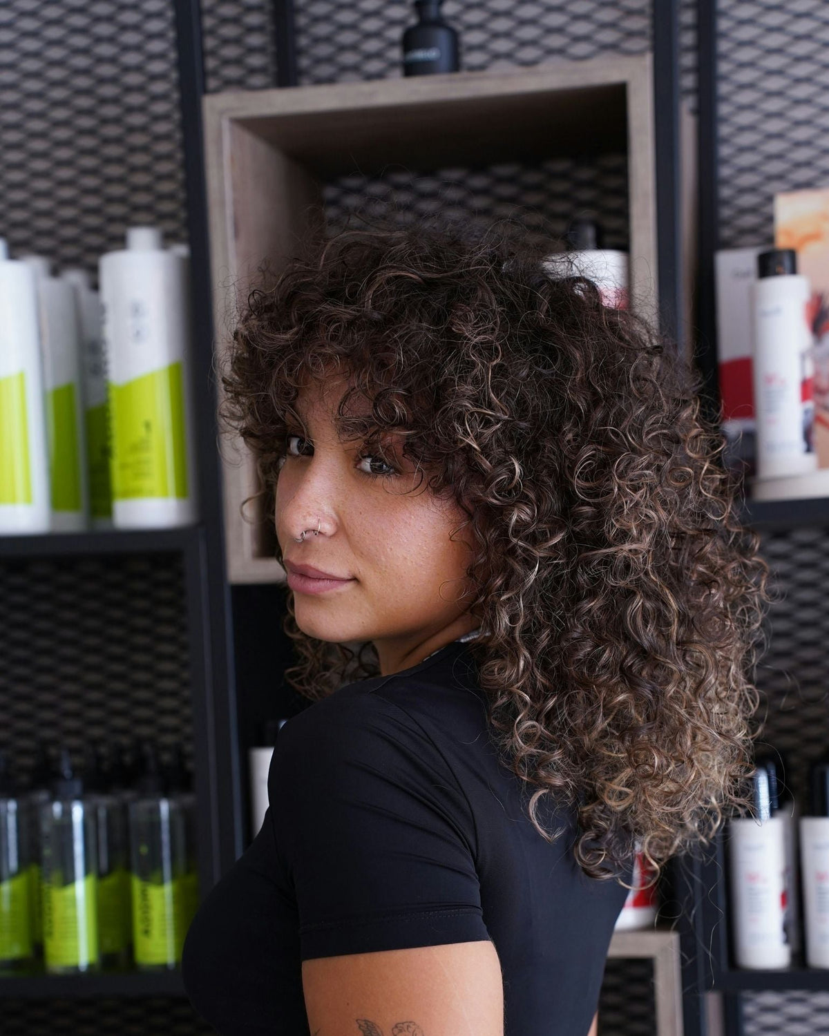 Woman with curly perm mullet looking over her shoulder in a salon with product shelves in the background
