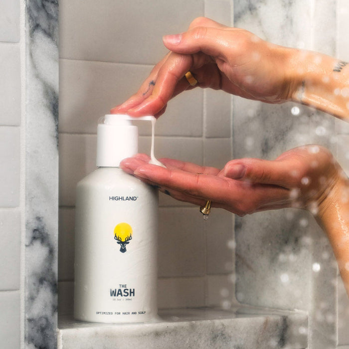 Hands pressing pump dispensing cleanser from bottle labeled HIGHLAND, THE WASH, OPTIMIZED FOR HAIR AND SCALP on shower shelf.