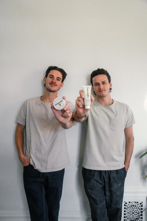 Two Highland co-founders holding a Glacial Clay Pomade tin and a Glacial Cream tube against a plain white wall