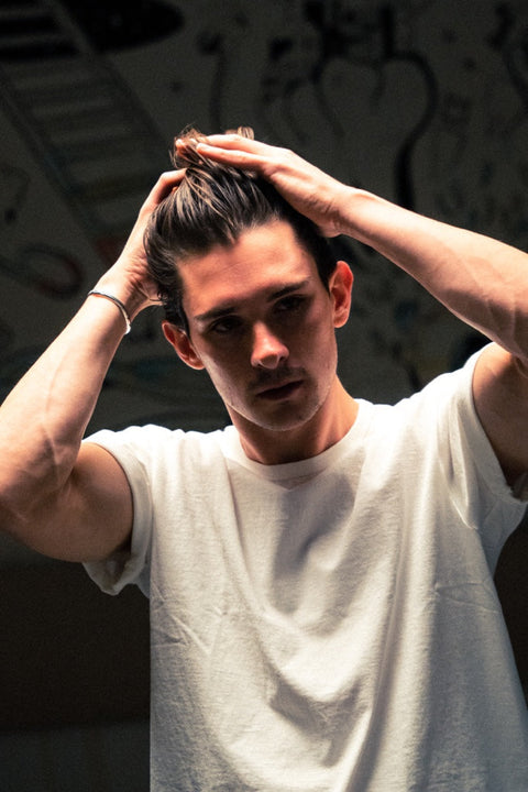 Young man in a white T-shirt pulling his hair back with both hands while styling it