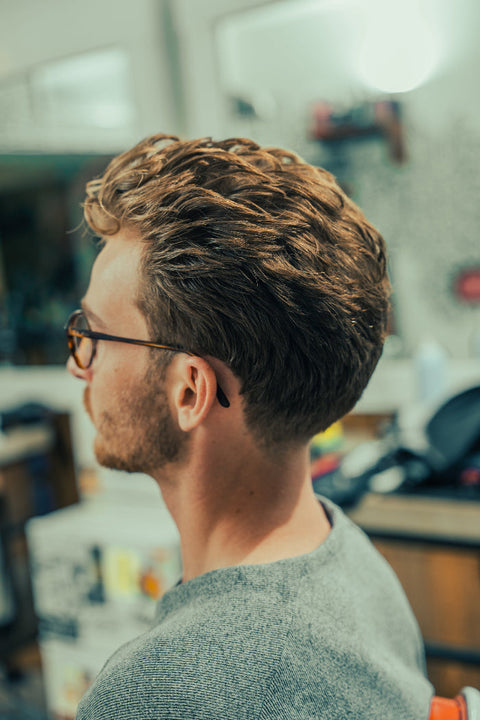 Man with low taper fade haircut sitting in a barbershop, side view showing textured top and tapered neckline