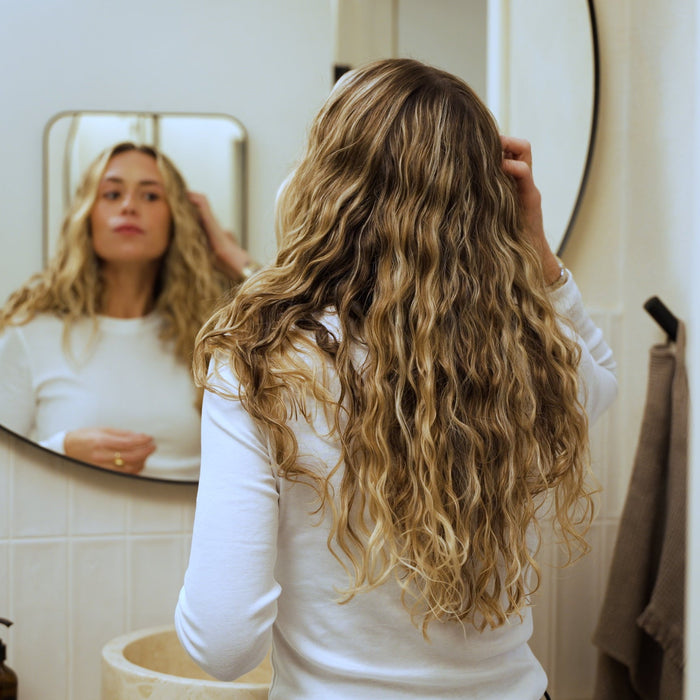 Woman in front of a bathroom mirror looking at her long curly hair