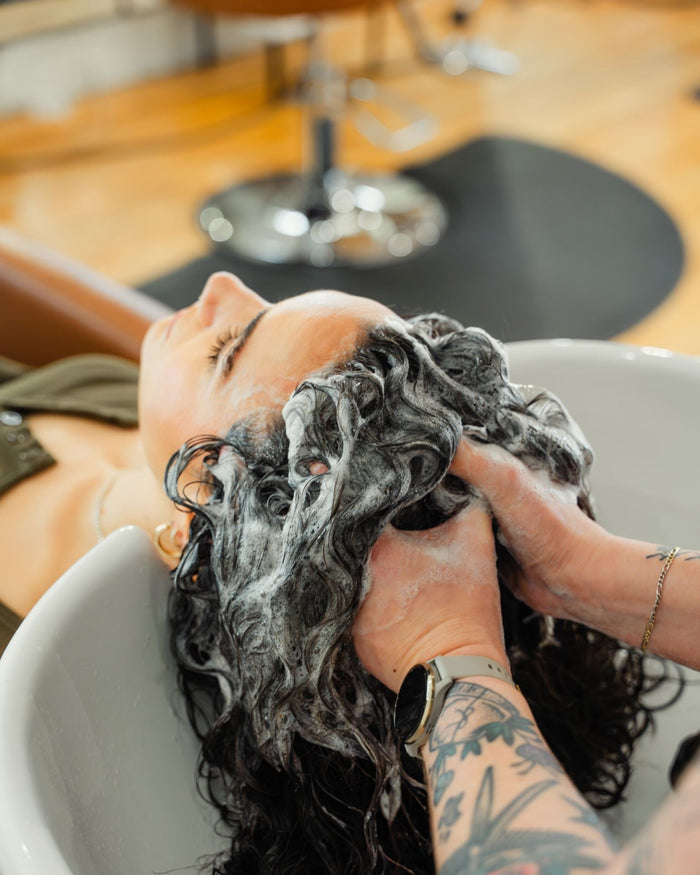 man washing woman curly hair in sink