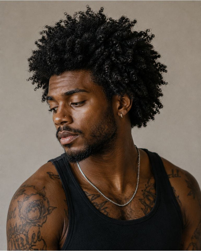 Man with defined natural Type 4 coily hair and tattoos looking away from the camera against a soft neutral background.