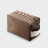 Angled view of the Highland Dopp Kit showing its brown water-resistant case, zipper, and carry handle on a light gray background