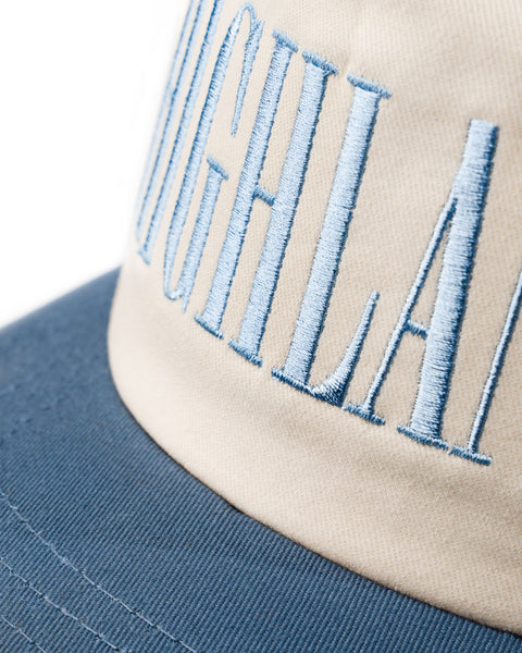 Beige and blue embroidered baseball cap with stitched letters 'HIGHLAND' on the front panel.