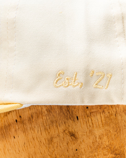 Cream hat hem with gold embroidered Est, '21 on fabric