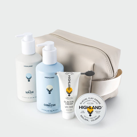 Angled view of Highland Dopp Kit showcasing its Mocha Cream zippered design and handle with toiletries on a light background