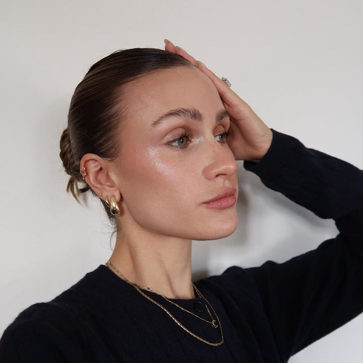 Woman with a bun and minimal makeup wearing a black cardigan against a plain background