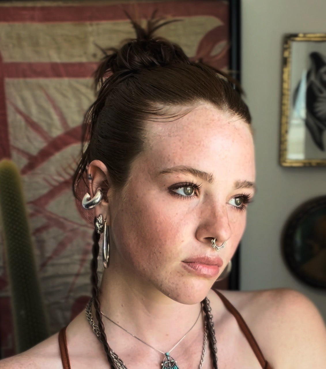 Close-up portrait of a young woman with freckles, green eyes, septum ring and multiple earrings, braided hair, looking right.