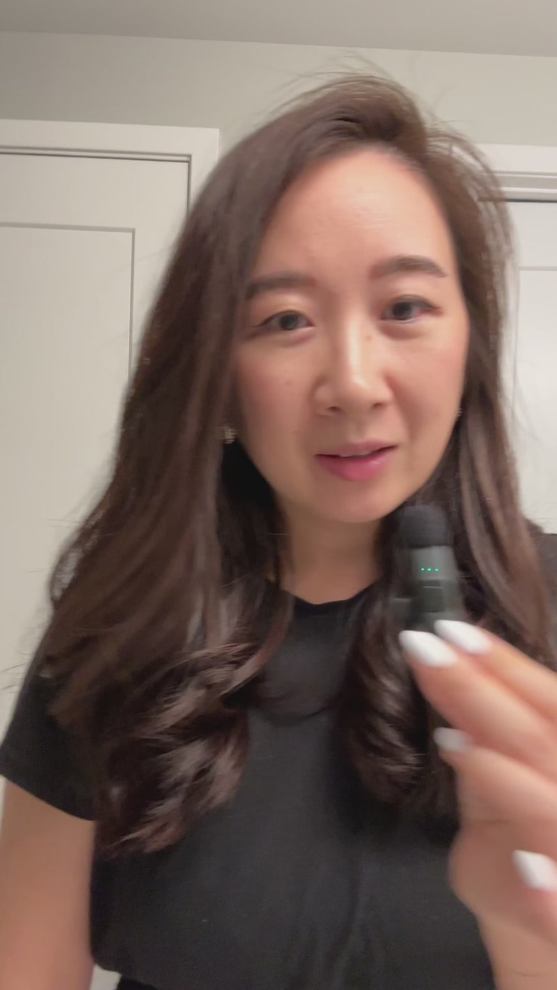 Person holding a small black applicator near their face; long dark wavy hair and white nails.
