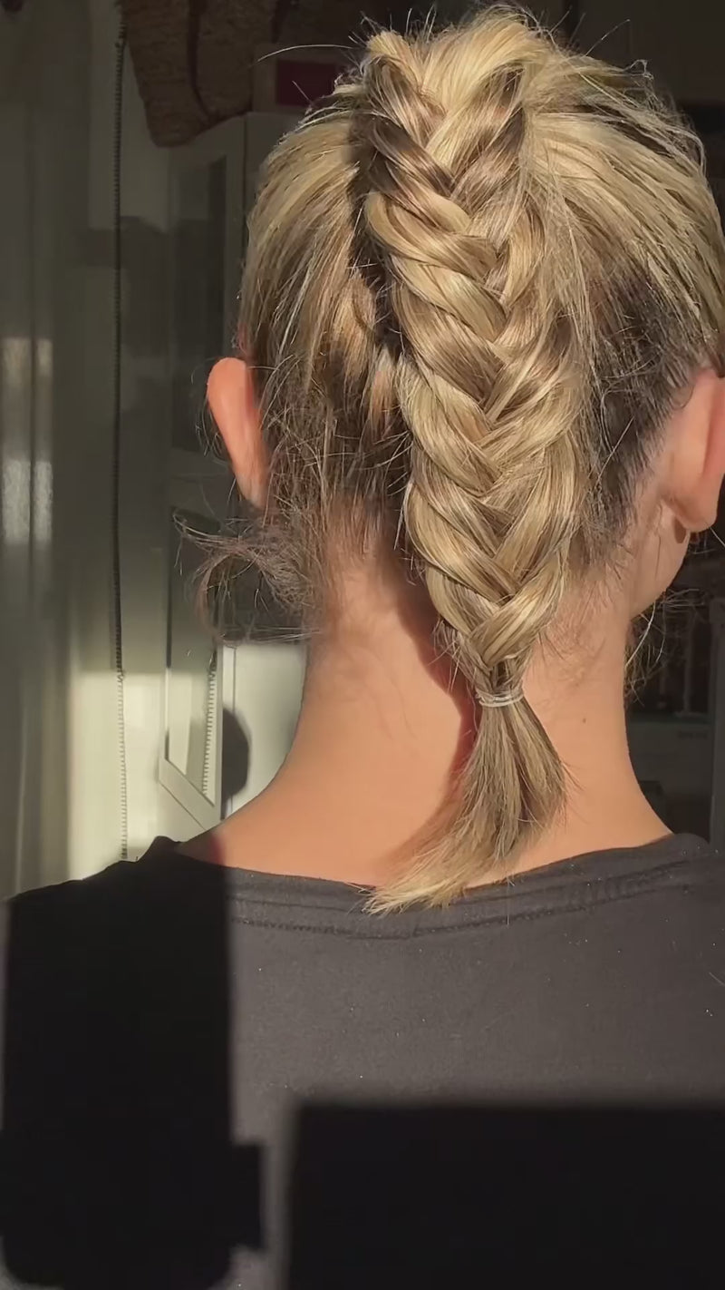Back view of a tight French braid on blonde hair secured with a small clear elastic