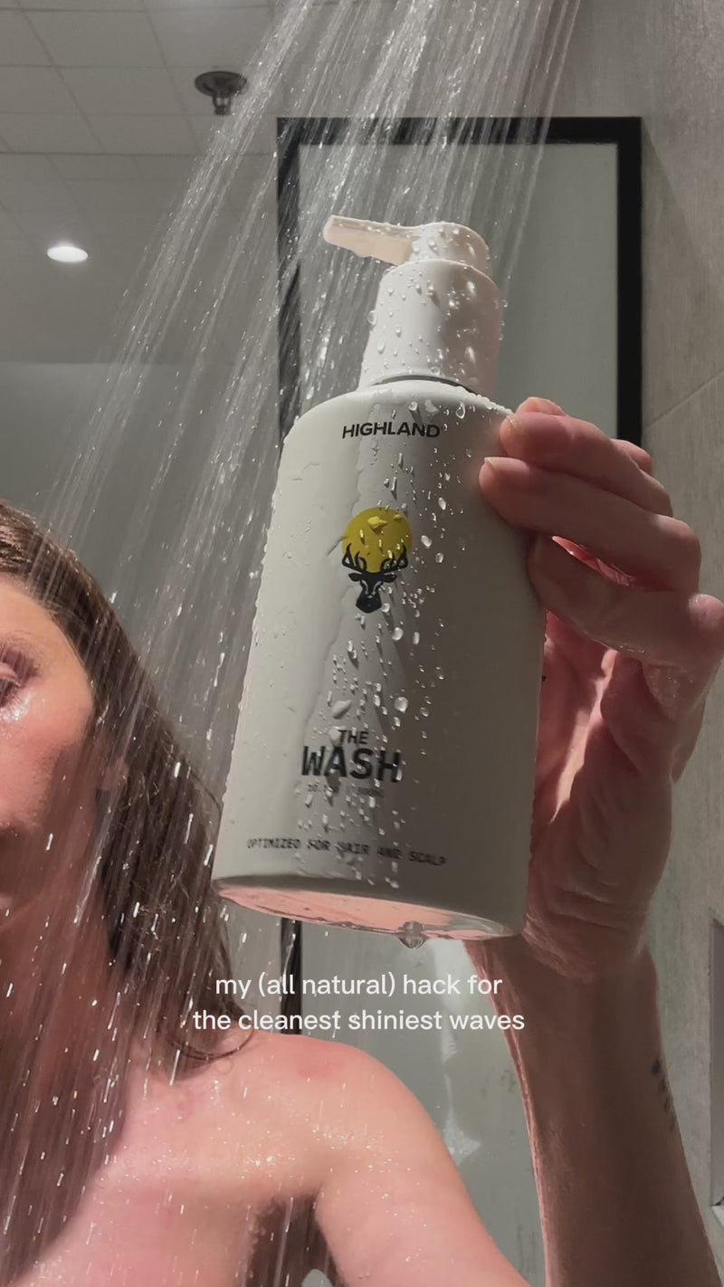 Hand holding HIGHLAND bottle labeled THE WASH under shower; my (all natural) hack for the cleanest shiniest waves