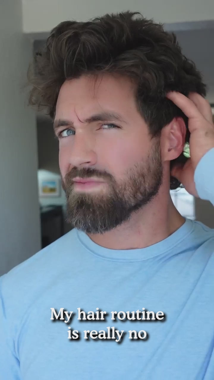Bearded man in light blue shirt touching his hair; caption reads 'My hair routine is really no'.